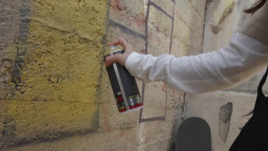 A woman with brown hair is spraying yellow paint on a wall
