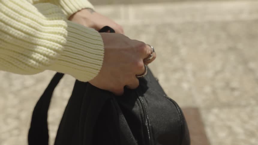 A pair of hands takes down a backpack and lays it on the sidewalk opens it up and takes out one of several spray paint cans