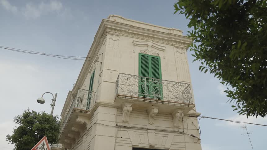 A white threestory building with green shutters and a balcony