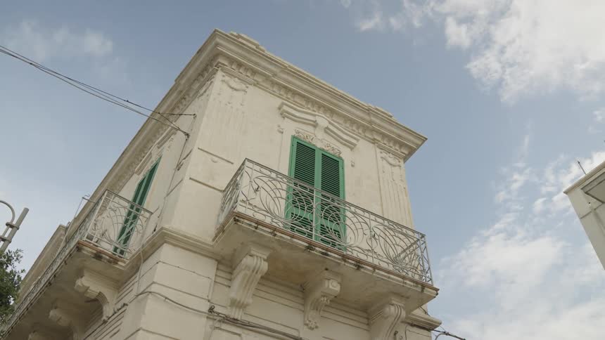 A white threestory building with green shutters and a balcony
