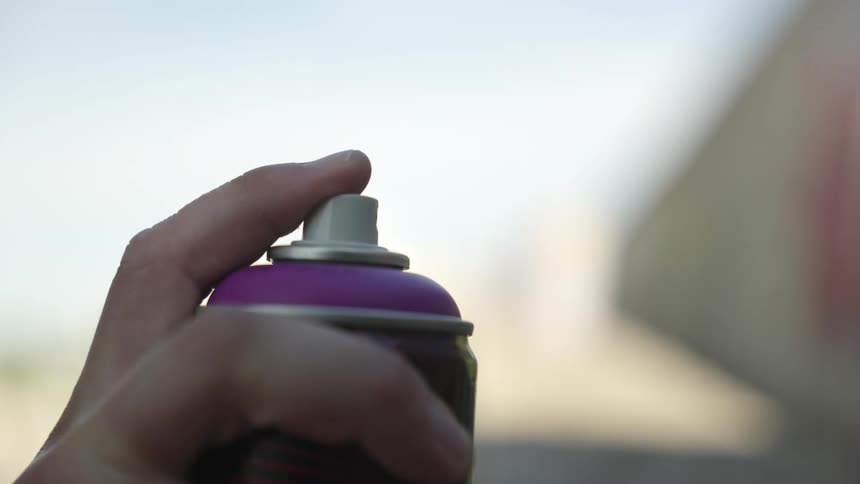 A finger is pressing down on the nozzle of a purple spray paint can