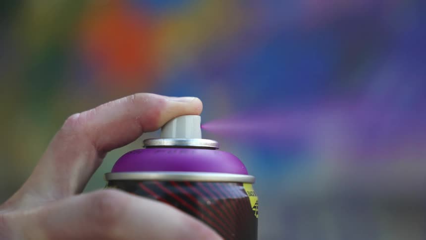 Hand pressing the cap of a purple spray paint