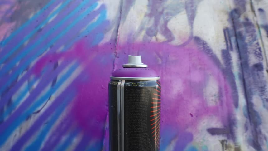 Closeup of a spray can in front of a vibrant graffiti wall with shades of blue and purple