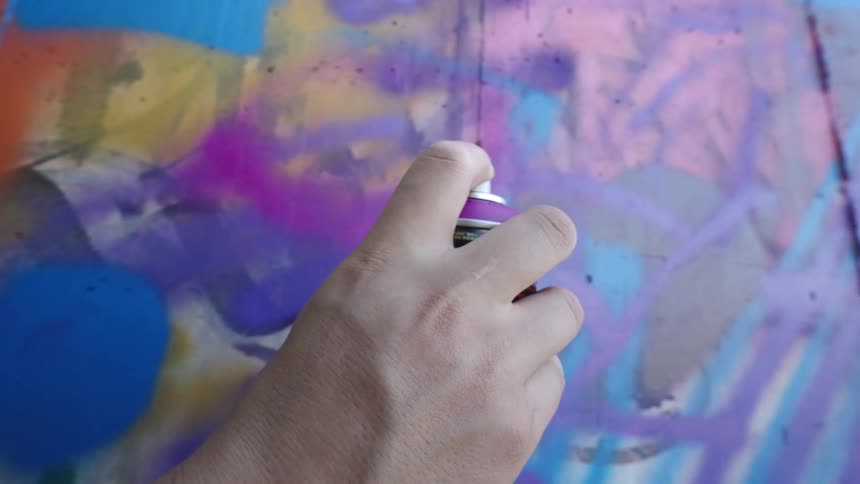 A hand holding a spray can and spraying paint on a wall