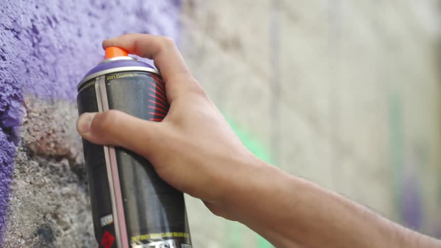Hand holding a spray paint and graffitiing a wall