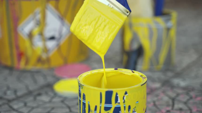 Hand holding a paintbrush dipped in yellow paint