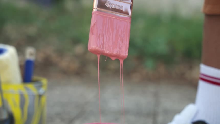 Hand holding a paintbrush dipped in pink paint