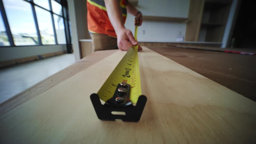 A construction worker is measuring a piece of wood with a tape measure