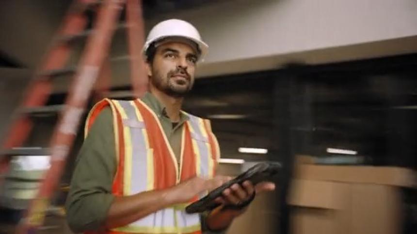 Man wearing hard hat and high visibility vest holding a tablet at a construction site