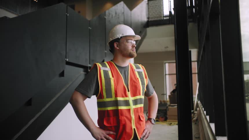 Man in protective vest helmet with hands on waist watching