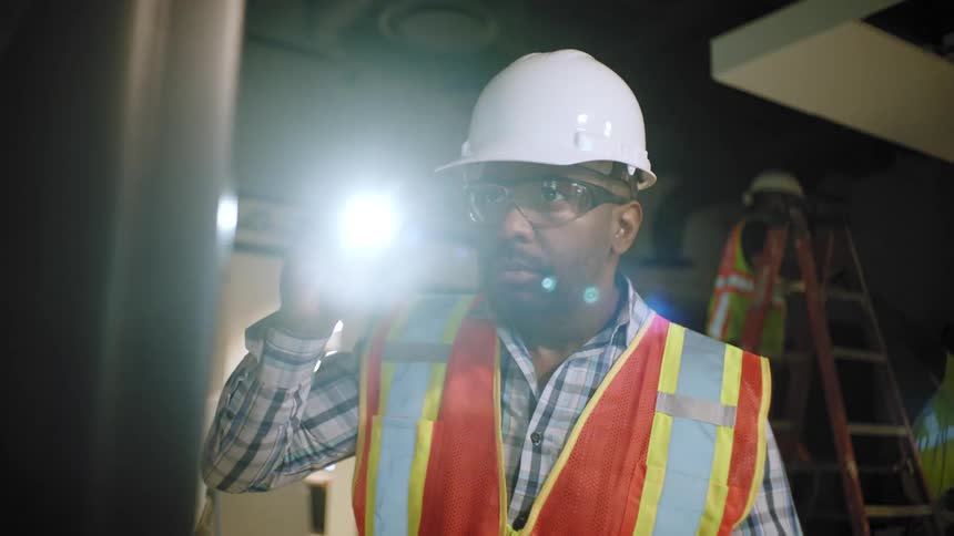 Man wearing helmet and vest holds an inspection flashlight