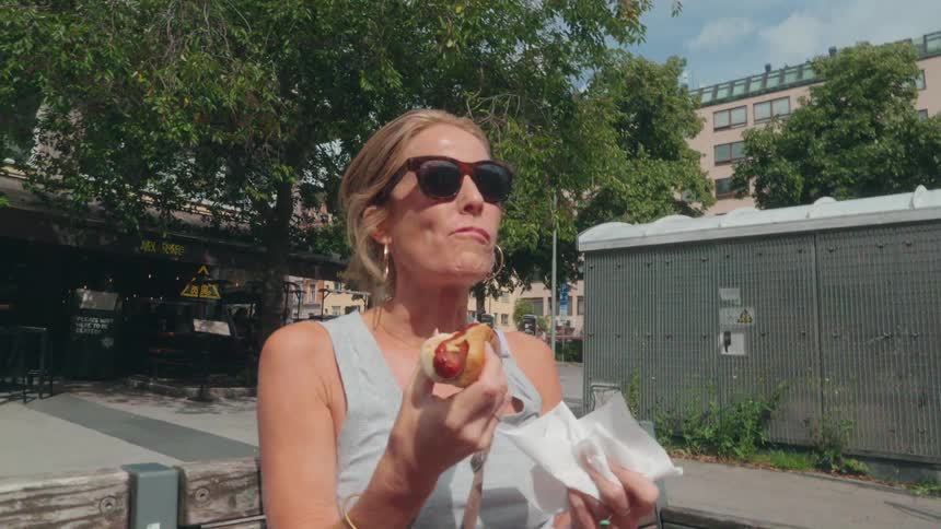 A woman is eating a hotdog outside