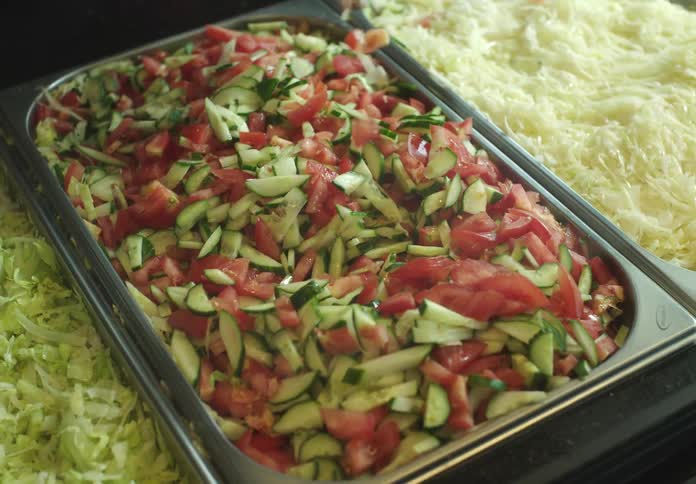 Closeup of a persons hand picking diced vegetables from a metal tray in a restaurant