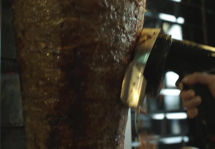 A hand using a machine to cut off slices of kebab meat