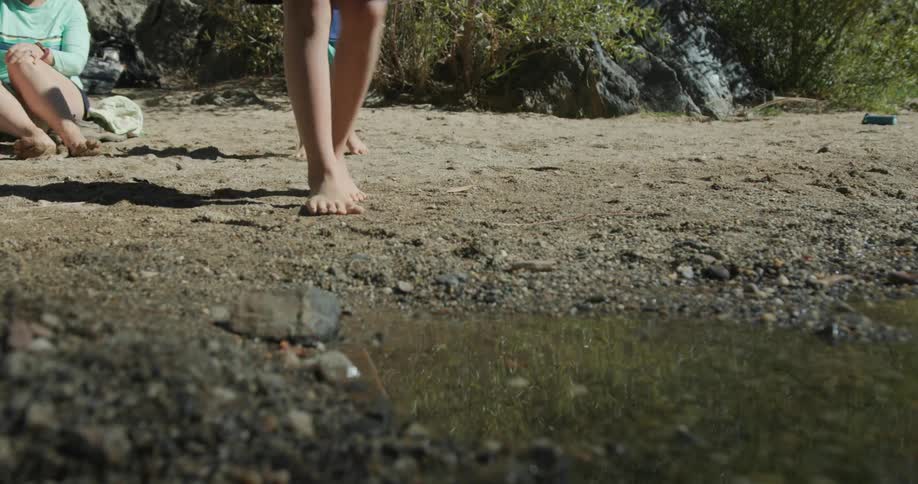 Legs of a child walking towards a lake and throwing mud