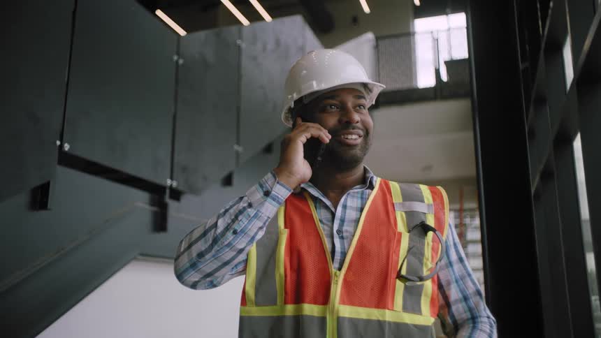 Man in helmet and vest in indoor space talking on smartphone