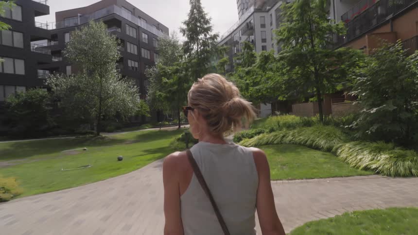 View of a woman from behind walking in a city with buildings and trees around