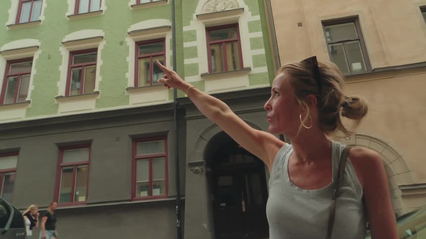 Blonde woman pointing finger up while standing in a classic urban city
