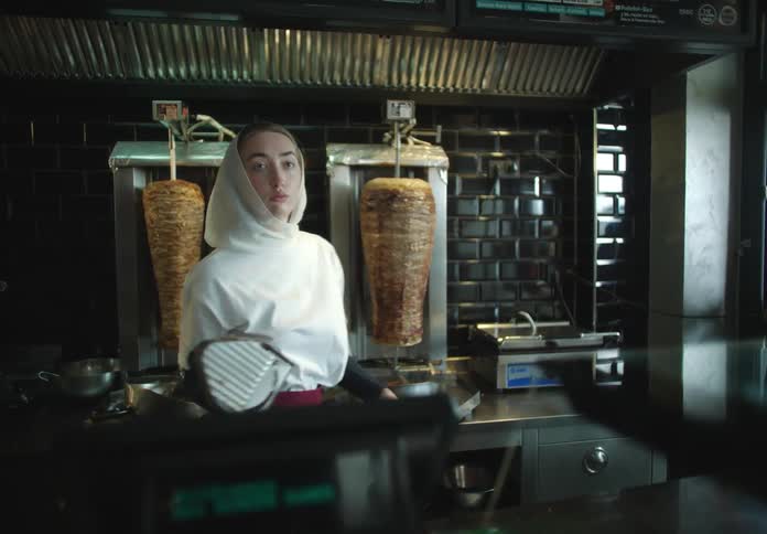 A young woman working in a kebab shop turns around facing the customer side