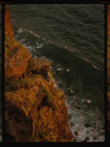 A dramatic coastal scene with crashing waves against a rocky cliff face bathed in warm sunlight