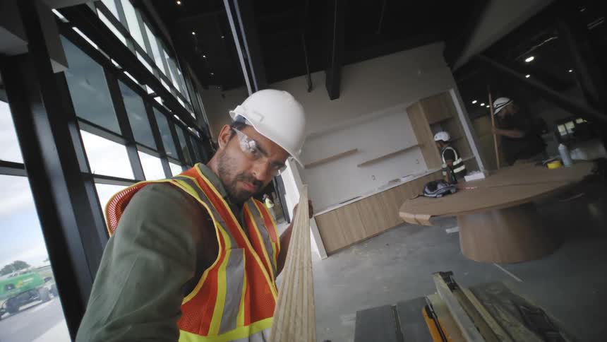 Man cuts wood on a table saw and carries it to another area of the construction site