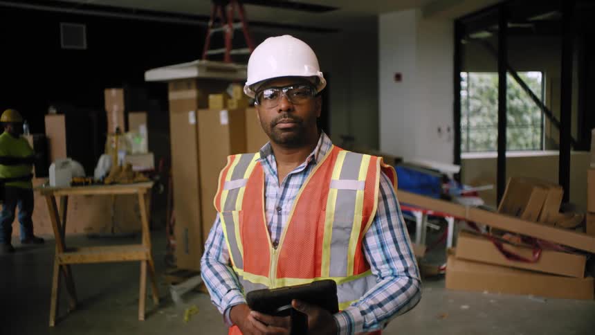 Portrait of a man wearing a hard hat and high visibility vest holding a tablet at a construction site