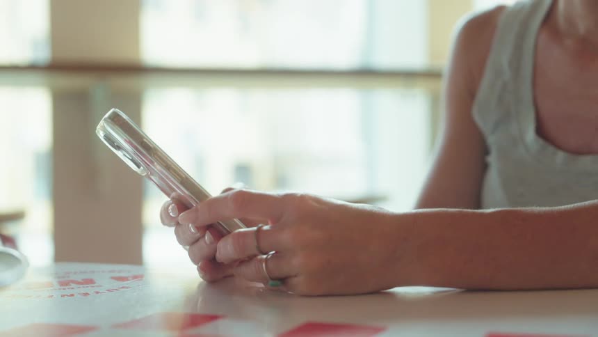 Hands of a woman sitting at a table using an iphone
