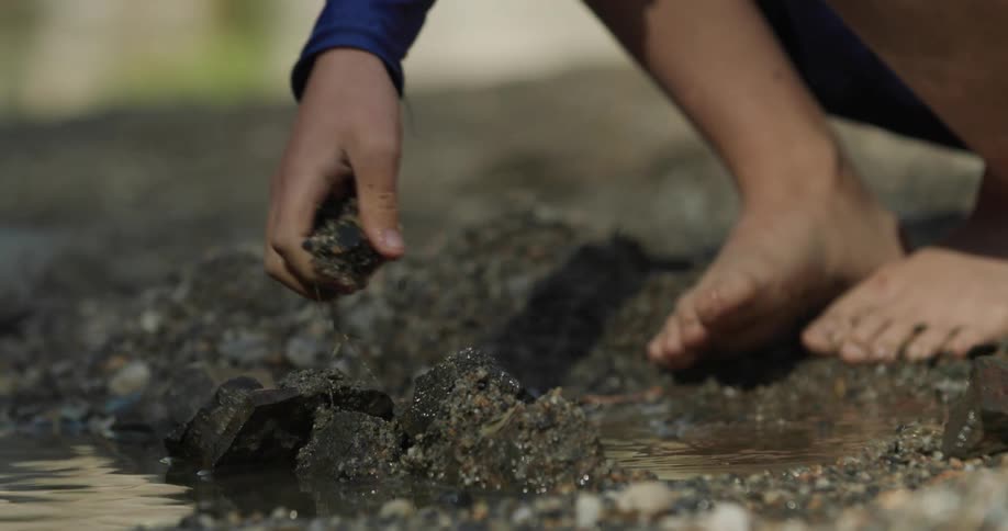 Hand of a child playing with clay at the edge of a lake