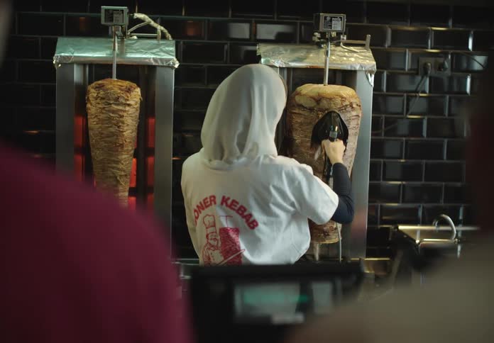 Two people watching a woman in a white sweatshirt cutting slices of roast beef in a restaurant