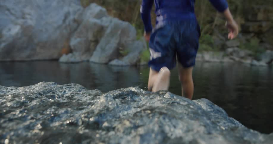 A boy in blue jumping into the water from a rocky surface