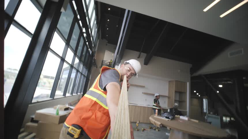 Man with protective helmet inside a company holding a wooden slat and passing it through a machine