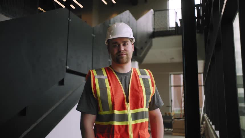 Portrait of a man in a white helmet and a signaling vest at a construction site