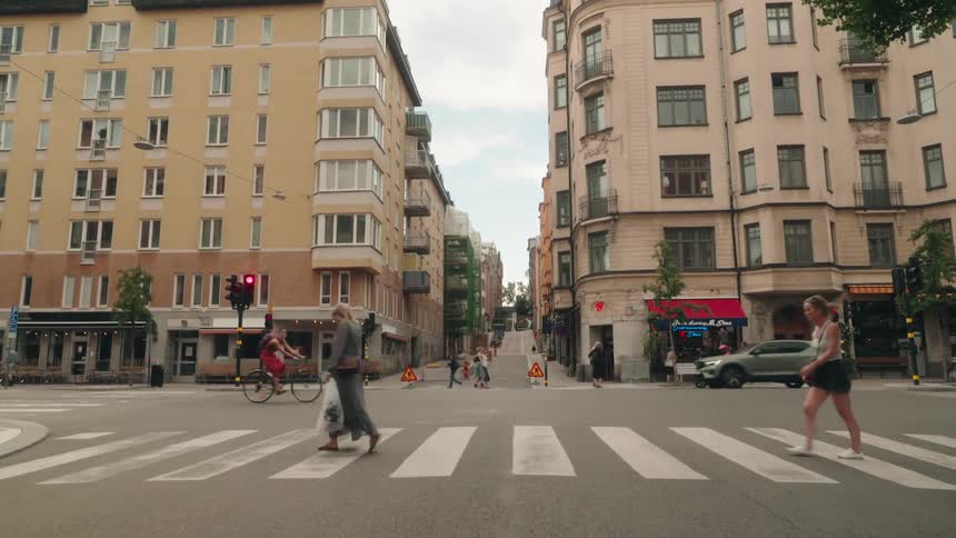 A person crossing a street at a crosswalk in an urban setting with tall buildings on either side and a cyclist passing by on the left
