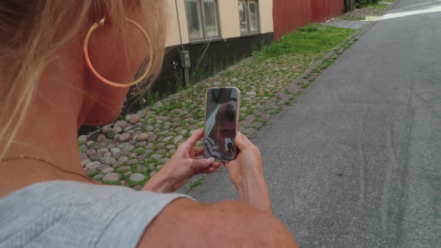 Blonde woman with hoop earrings and a gray top has a video call on smartphone standing on the street