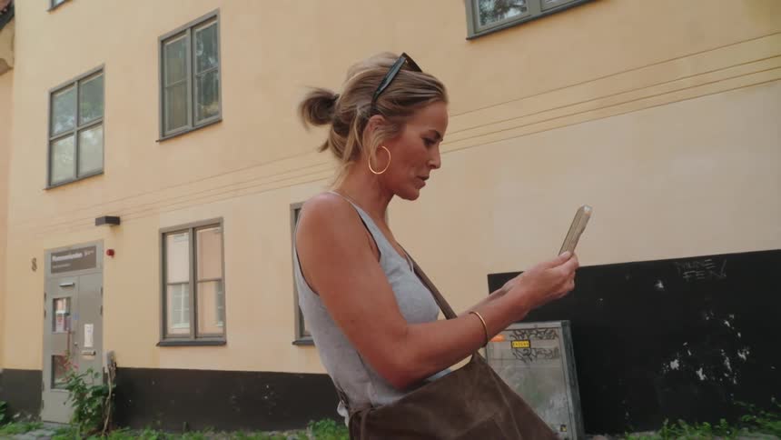 A woman standing in a street talking and smiling while using a smartphone to make a video call