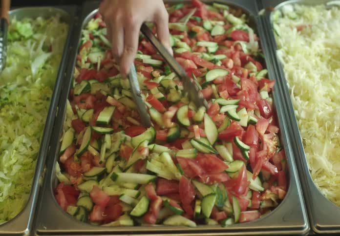 Hand with a spatula serving tomato and cucumber salad in a restaurant