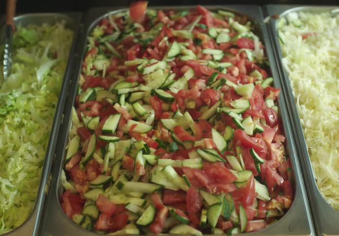 Hand holding a spatula and scooping tomato and cucumber salad