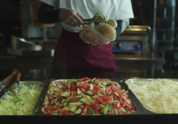 Hands of a woman putting together a snack by putting salad on a bun in a restaurant