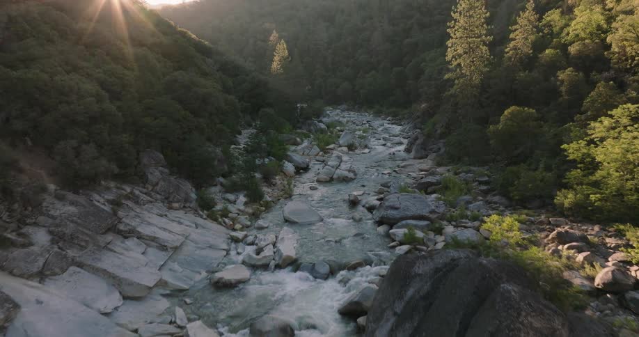 Landscape of a river flowing between rocks in surrounded by mountainous forests with the sun on the horizon