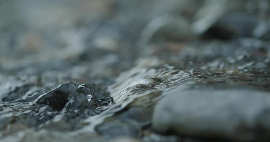 A closeup of a stream flowing over smooth wet stones