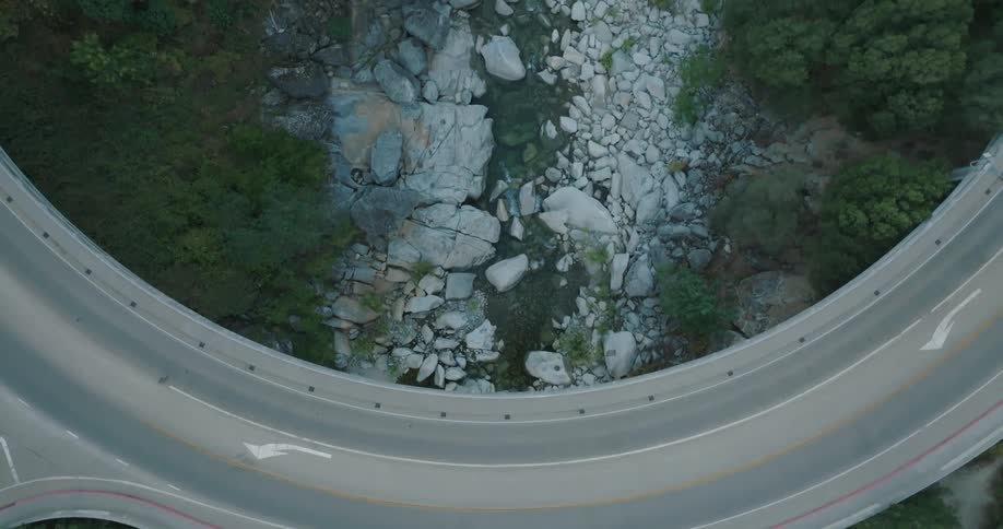 Aerial view of a curved road with double yellow lines above a rocky terrain with a river