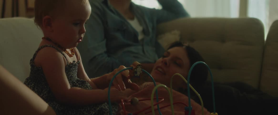 Parents with their daughter on the sofa with the father talking on the phone and the mother playing with their daughter