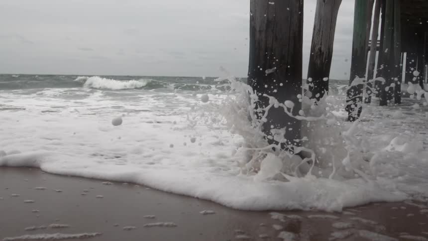 Water slowly incoming from the ocean and splashing on the pier's legs