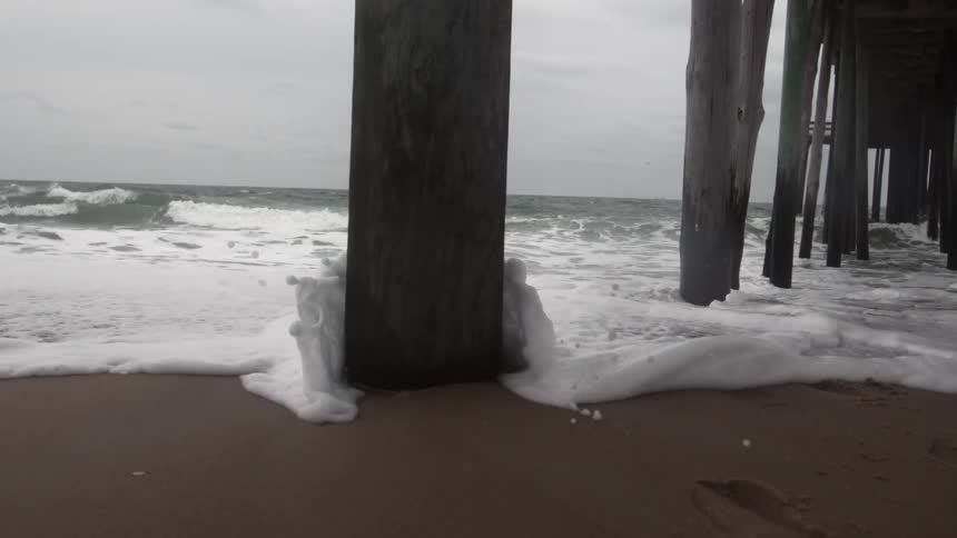 Water washing up on the beach underneath a dock