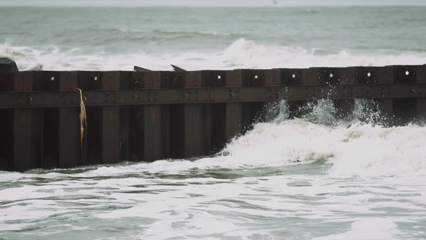 Ocean waves crash into a metal barrier