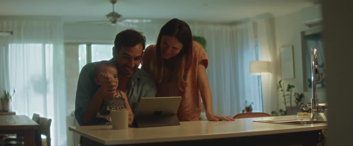 A mother father and young daughter together smiling and laughing at the tablet in front of them