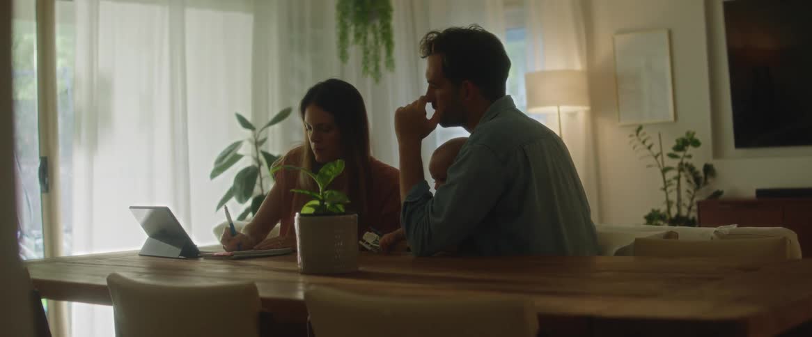A mother and father talking at the dining room table while the man holds their baby