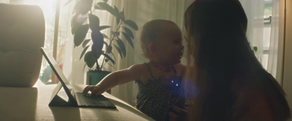A mother with her baby daughter using a laptop and hugging her