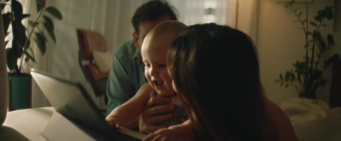 Parents smile as daughter plays with tablet in their home