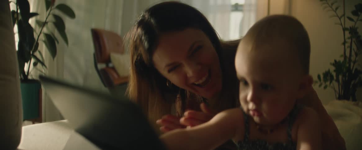 A mother clapping her hands for her baby daughter who is using a laptop on the sofa